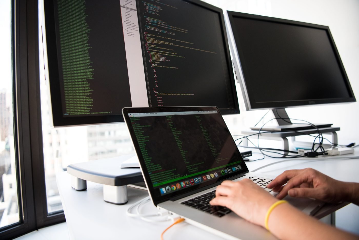 Developer coding on a laptop in front of multiple monitors