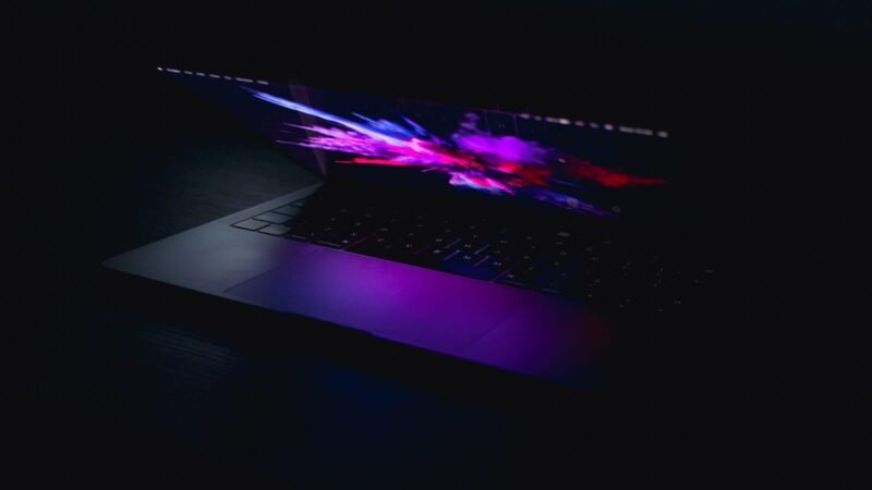 Open laptop glowing with colorful abstract light in a dark room