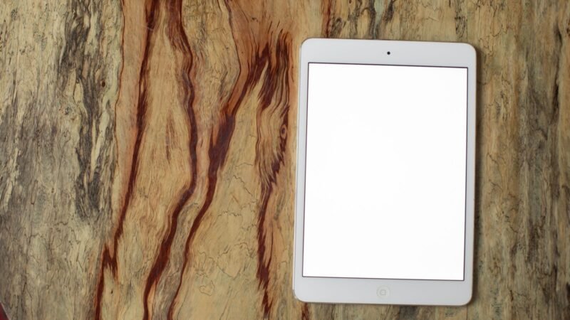 An earlier-generation white iPad mini lying on a wooden surface