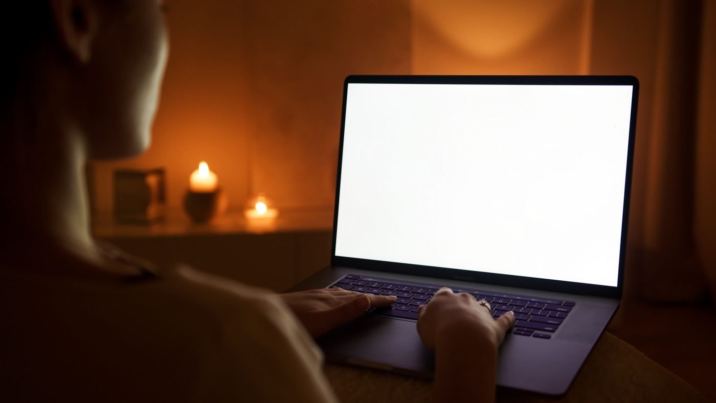 Person typing on a glowing laptop in a dim room at night