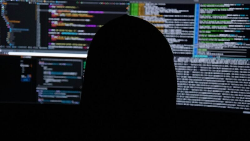 Silhouette of a person against multiple monitors displaying lines of code