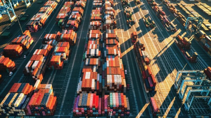 Stacked shipping containers at a harbor, representing military supply chain logistics