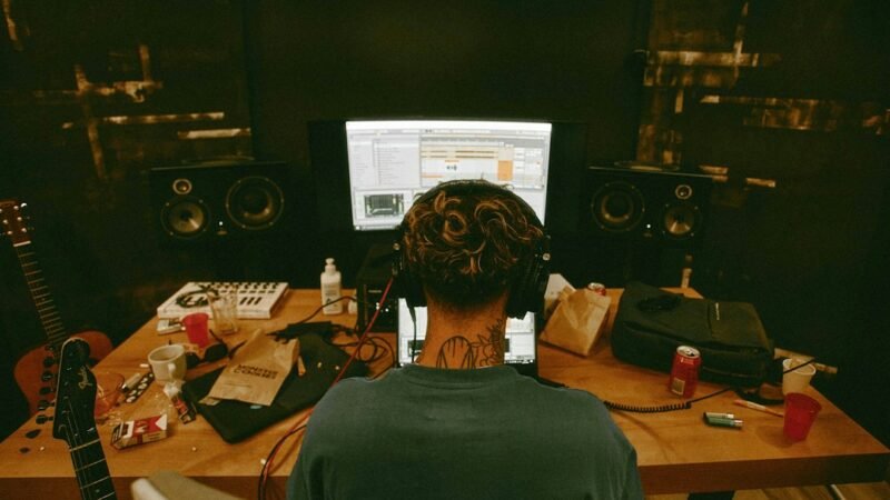 Man sitting at a desk with a guitar in a home recording setup