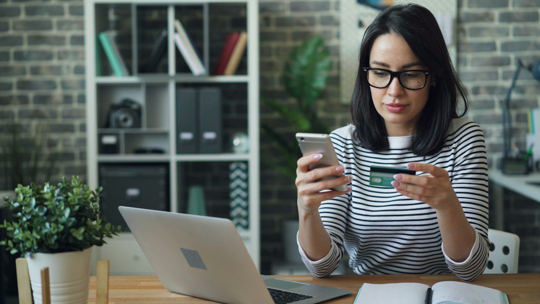 Person holding a credit card while using a smartphone for online shopping