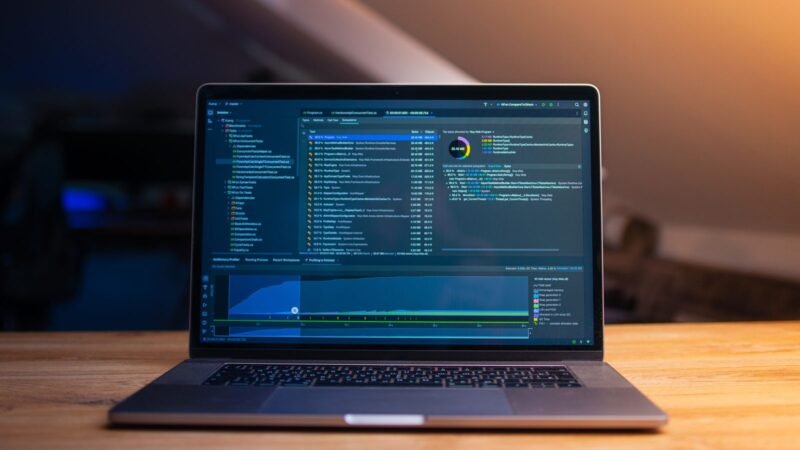 Laptop displaying lines of code on a wooden desk in a dimly lit room