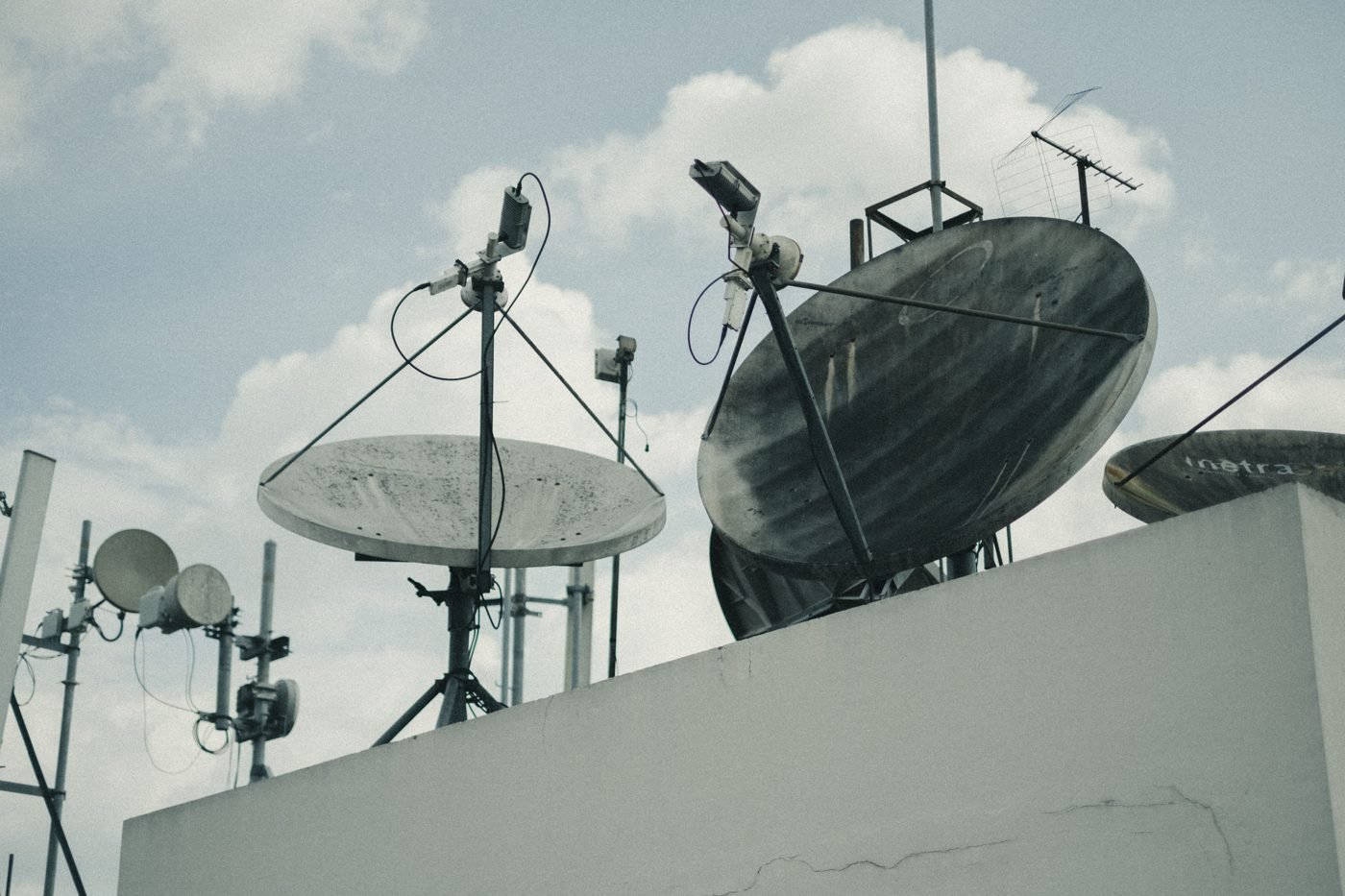 Satellite dishes and antennas on a rooftop under a cloudy sky