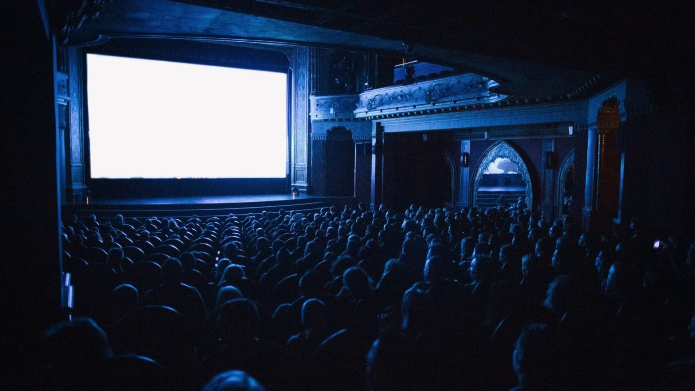 Audience seated in a dark movie theater facing a glowing screen