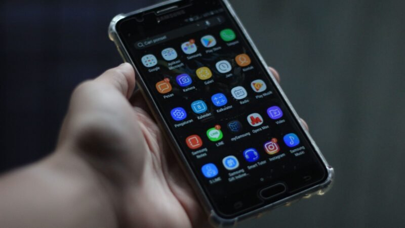 Hand holding an Android smartphone showing its home screen