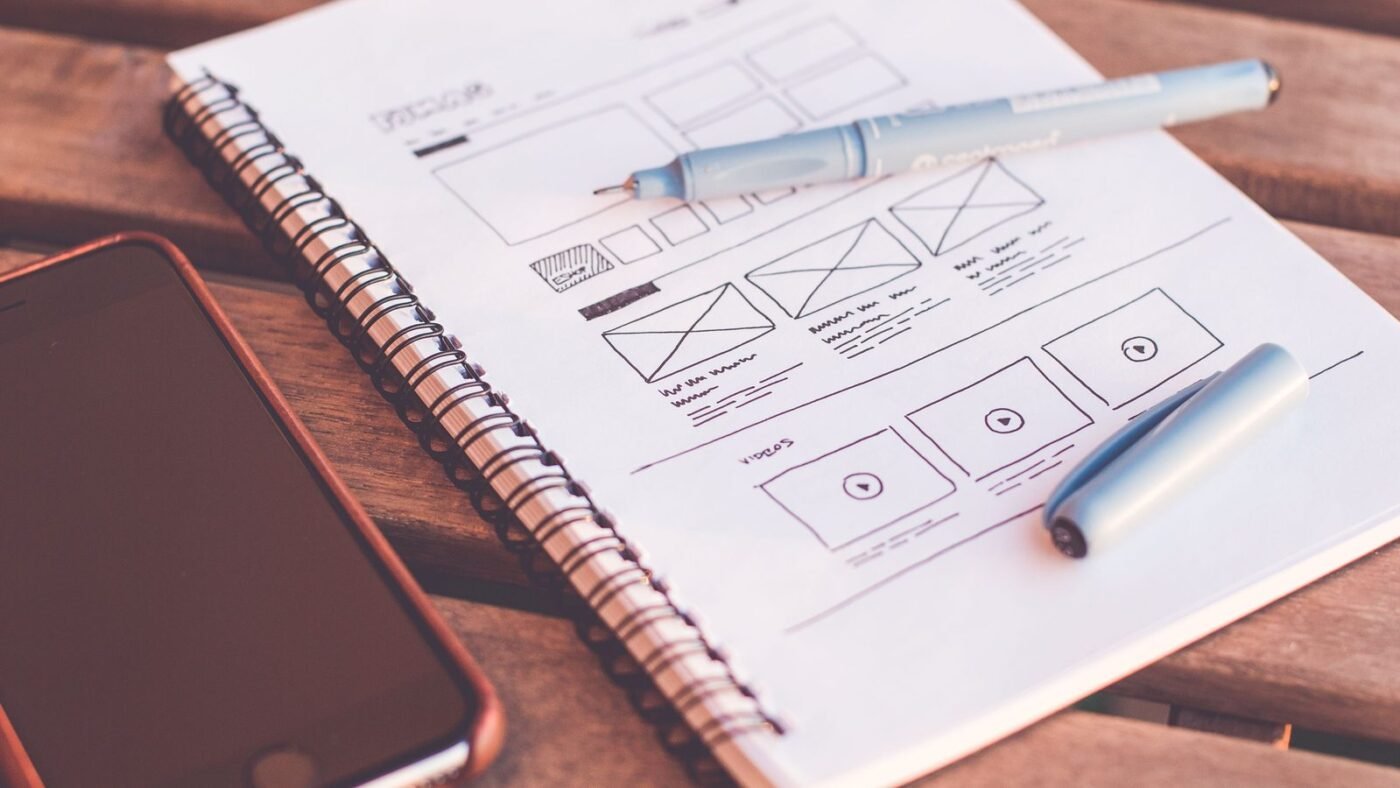Notebook with app wireframe sketches next to a smartphone and pen on a wooden desk