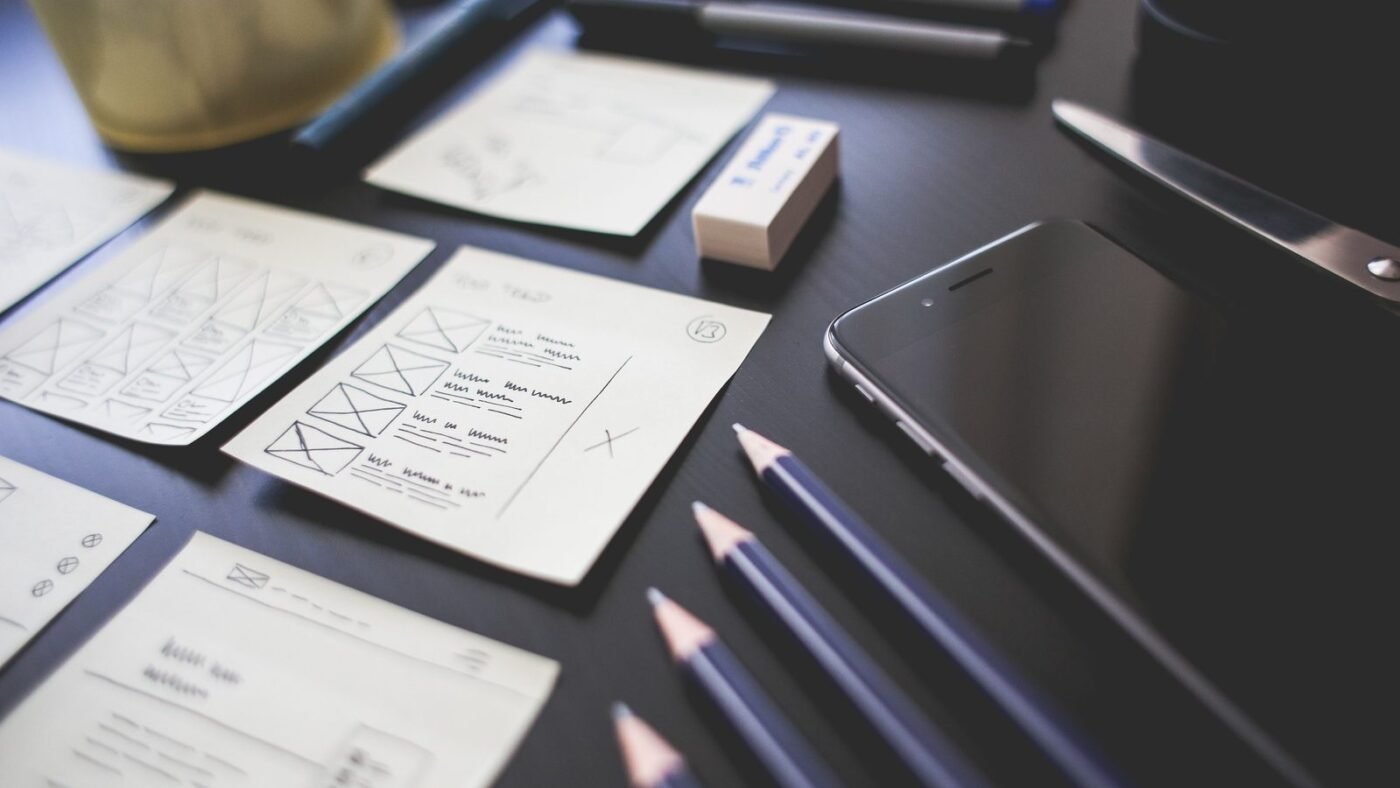 Desk with UI design plans, pencils and a smartphone