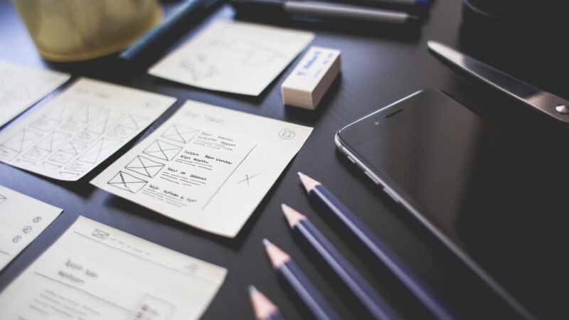Desk with UI design plans, pencils and a smartphone