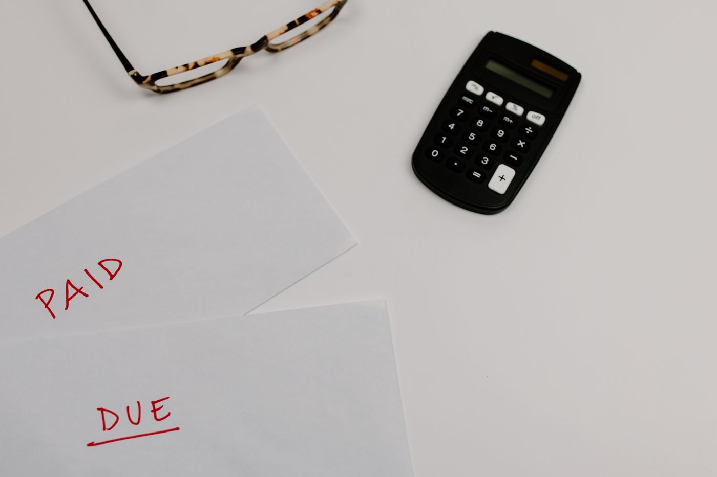 Papers marked Paid and Due beside a calculator and glasses