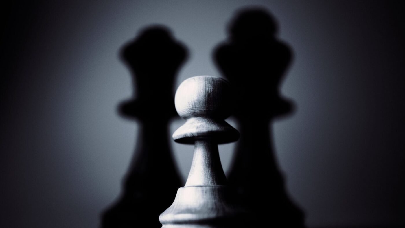 White chess pawn in front of dark chess pieces in dramatic lighting