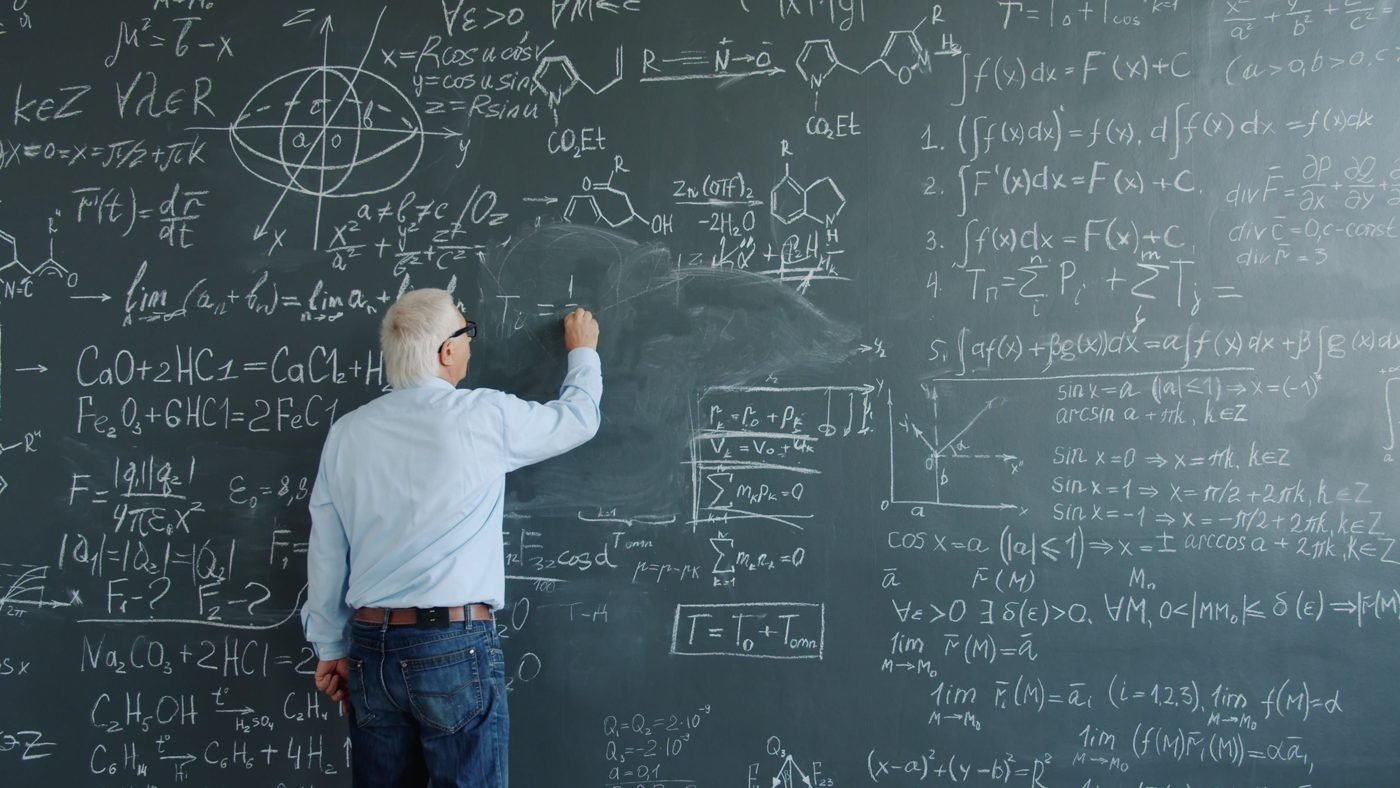 Man writing math equations on a large chalkboard