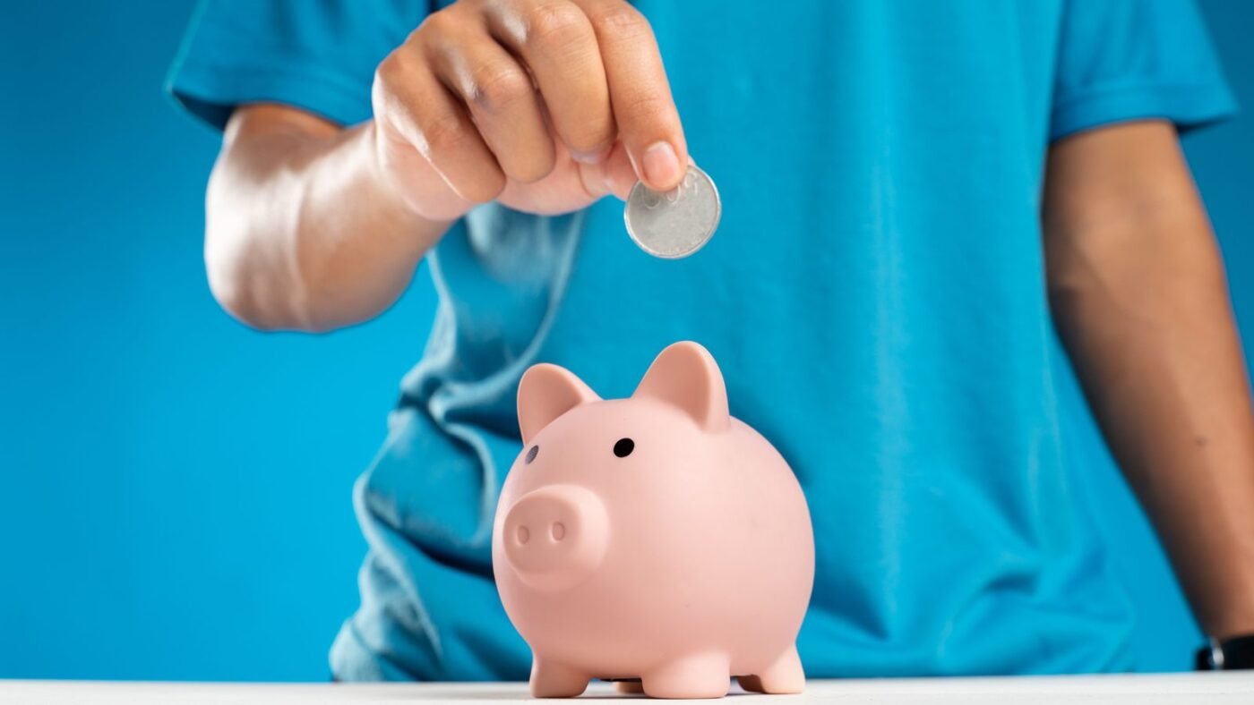 Hand dropping a coin into a pink piggy bank