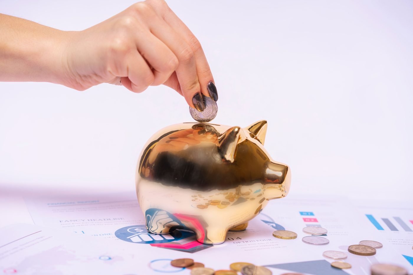 Hand placing a coin into a golden piggy bank beside financial charts