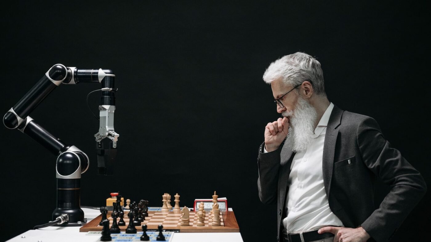Thoughtful older man standing beside a robotic arm at a chess board