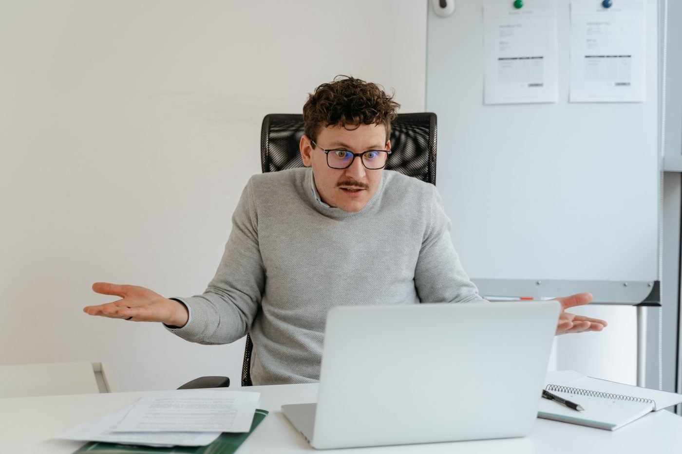 Confused man shrugging at his laptop at an office desk