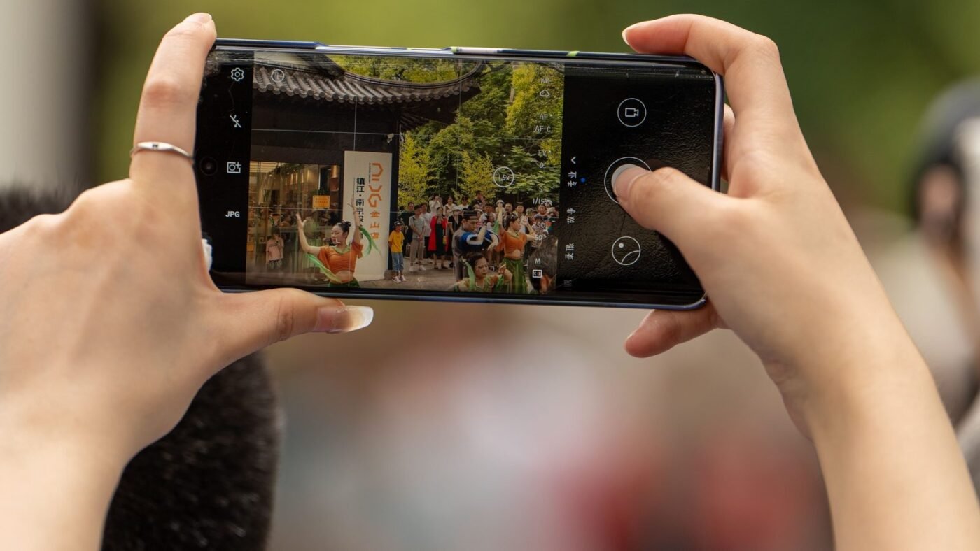 Hands holding a smartphone to take a photo of a street scene