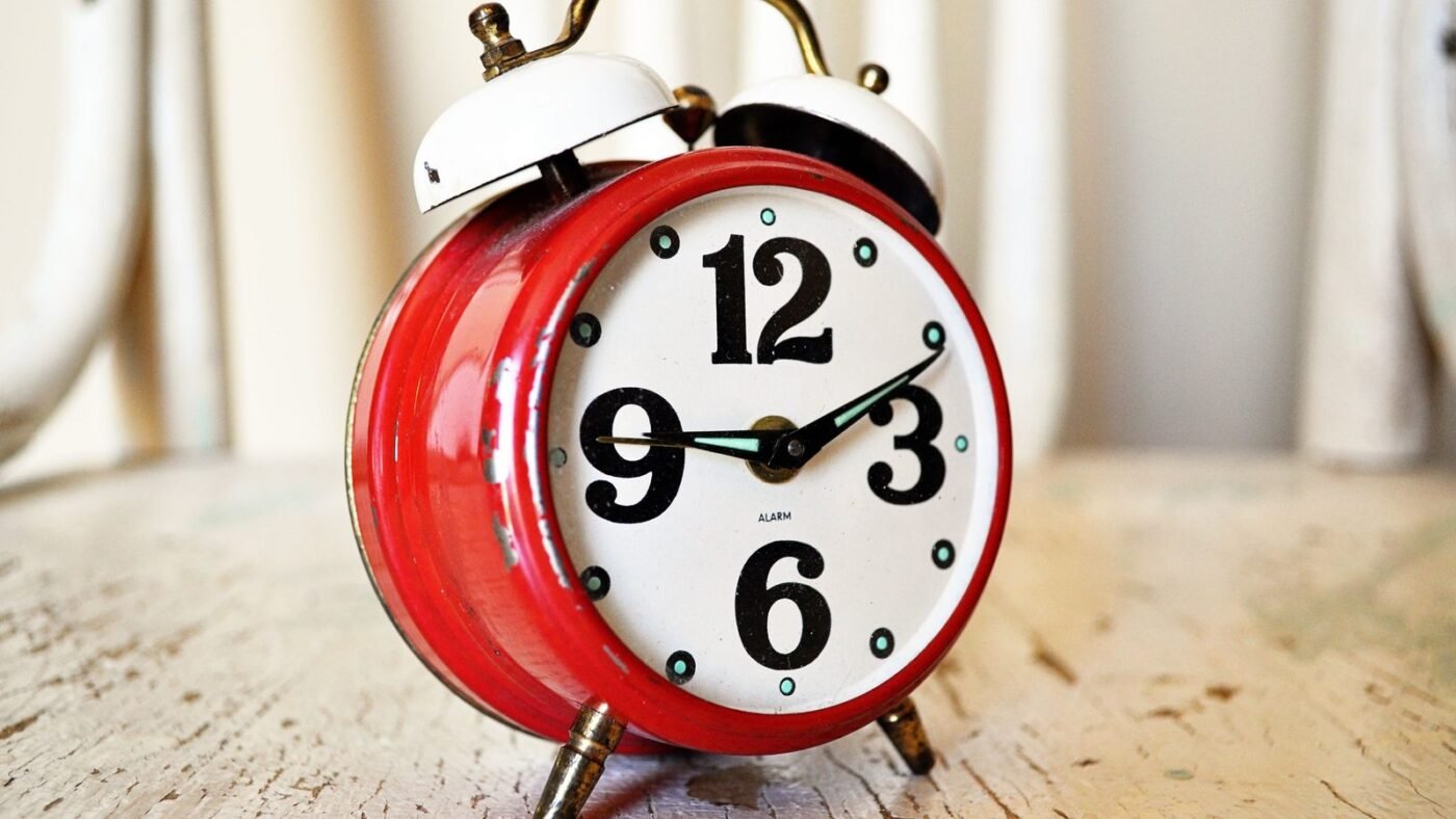 Vintage red alarm clock on a rustic wooden surface