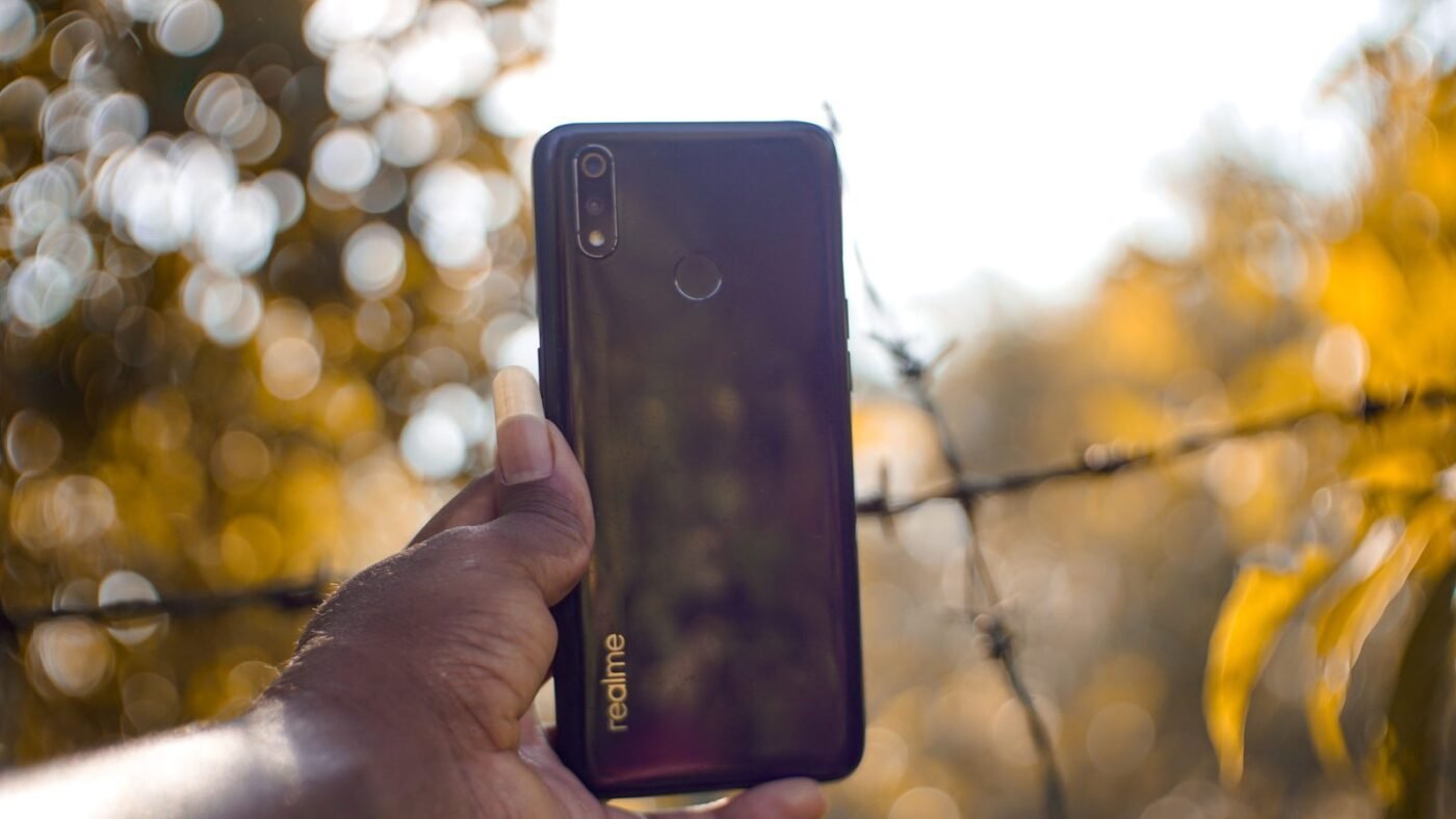 Hand holding a smartphone outdoors with warm sunlit bokeh in the background