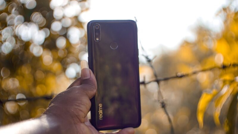 Hand holding a smartphone outdoors with warm sunlit bokeh in the background