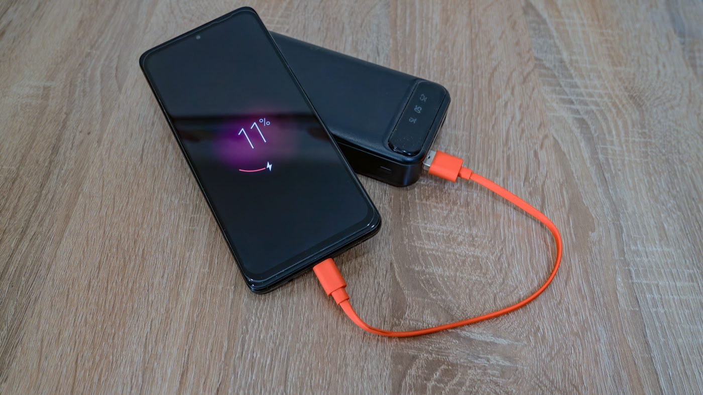Smartphone charging from a power bank with an orange cable on a wooden table