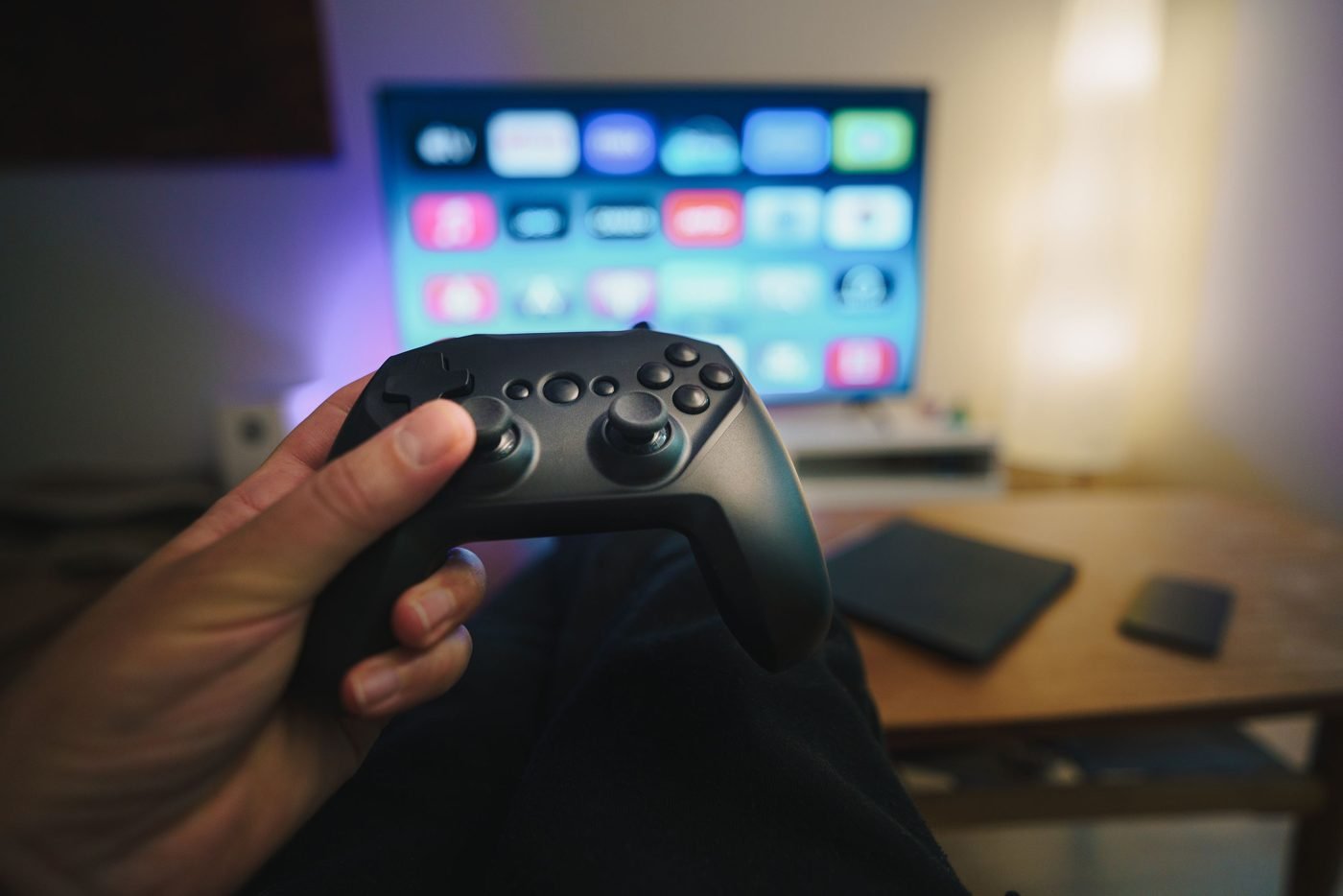 Person holding a gaming controller in a living room with a TV
