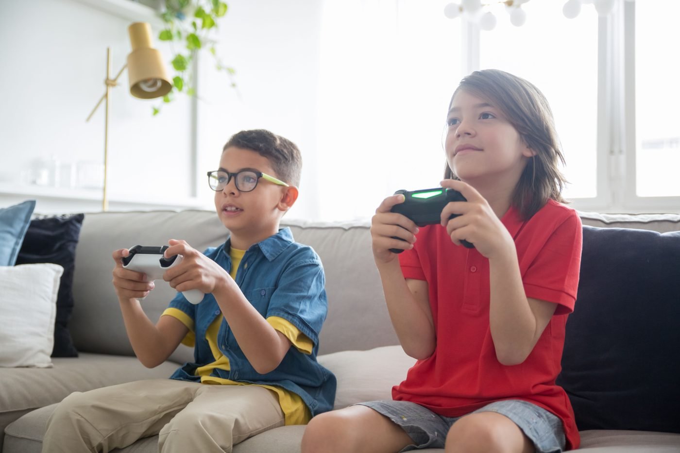 Two kids sitting on a couch playing video games with controllers